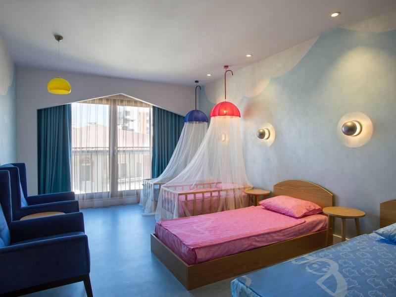 Camera d'hotel luminosa con due letti, poltrone e balcone con zanzariera.