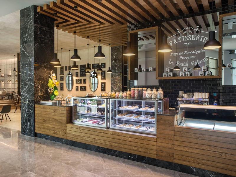 Caffè moderno con rivestimenti in legno, vetrine con pasticceria e illuminazione calda.