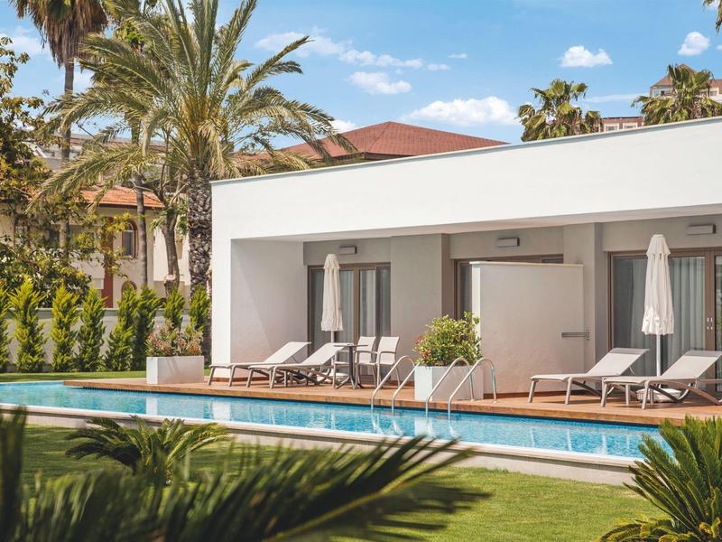 Bungalow moderno con piscina e lettini in un giardino tropicale.