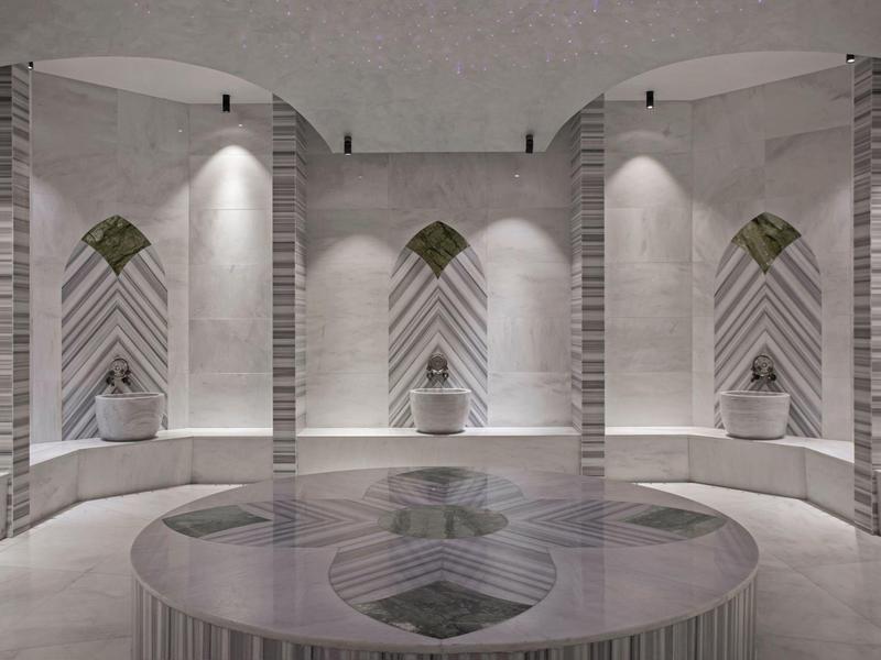 Hammam moderno con nicchie simmetriche, panche in marmo e vasca rotonda centrale