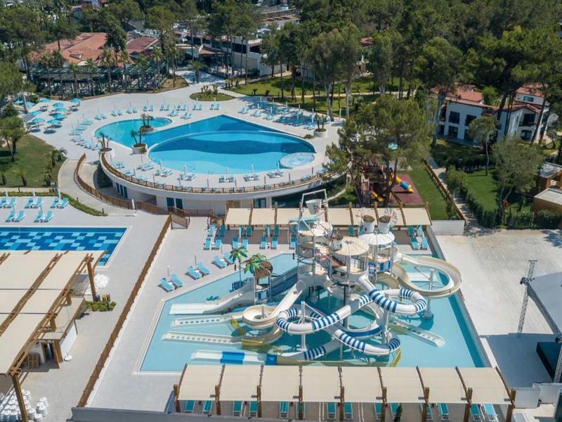 View of hotel pool area with multiple hot tubs and surrounding loungers in a green setting.