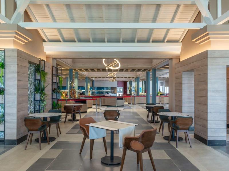 Modern hotel restaurant with wooden beam ceiling, tables, and comfortable chairs.