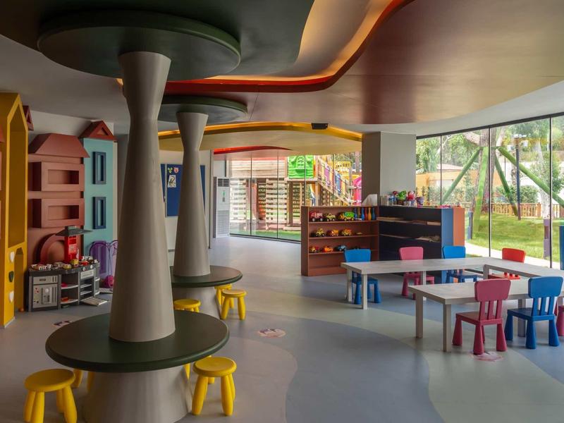 Bright, modern play area with colorful chairs, tables, and playhouses next to large windows.