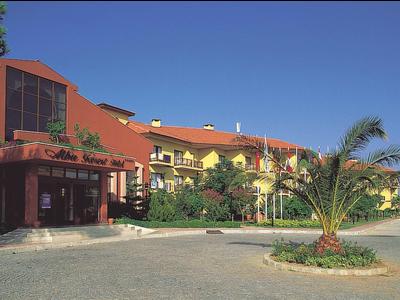Hotel with red and yellow buildings under clear blue sky next to a palm tree in a circular garden.