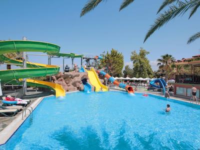 Großer blauer Pool mit grüner Wasserrutsche, gelben Rutschen und Menschen im Sonnenschein.