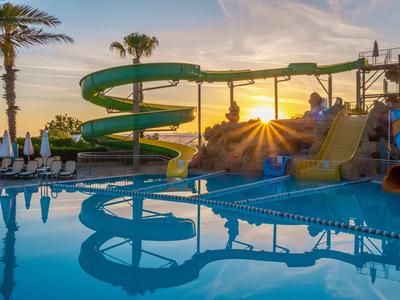 Water park with slides and palm trees at sunset next to a swimming pool.
