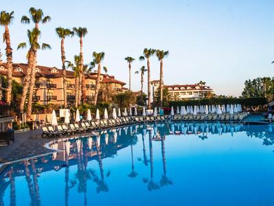 Resort pool with palm trees and sun loungers under clear blue sky.