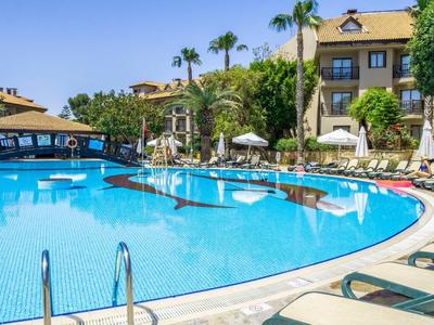 Resort swimming pool surrounded by sun loungers, umbrellas, and tropical palm trees under clear sky.