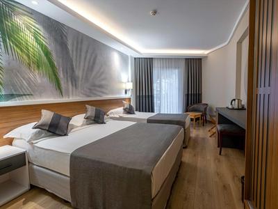 Modern hotel room with two beds, bedside tables, wooden flooring, and a large window with curtains.