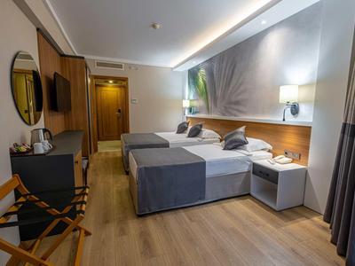 Modern hotel room with two beds, wooden floor, bedside lamps, and artwork on the wall.