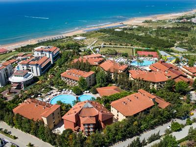 Große Hotelanlage mit mehreren roten Gebäuden, Pools und Nähe zum Sandstrand am Meer.