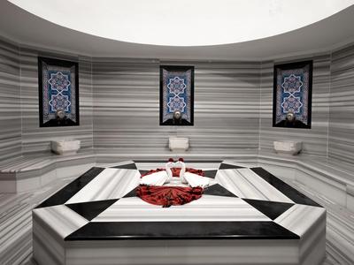 Modern gestaltetes Hamam mit Marmorbecken und Mosaikfenstern in sanften Grautönen.