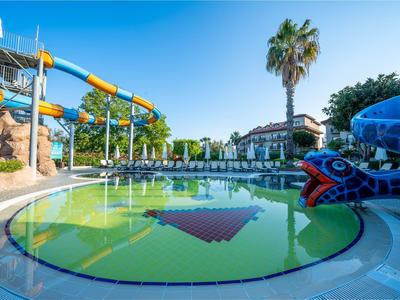 Außenpool mit Wasserrutschen und Palmen unter klarem blauem Himmel in einer Hotelanlage.
