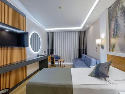 Modern eingerichtetes Hotelzimmer mit Bett, Sofa, TV und großem Fenster mit Vorhängen.