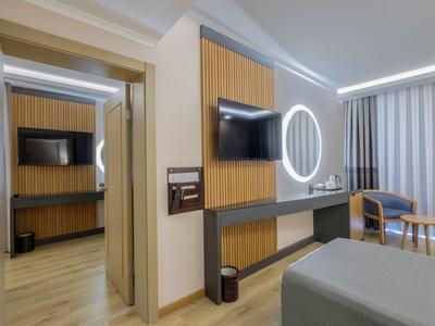 Modernes Hotelzimmer mit Holzvertäfelung, Wandfernseher und rundem beleuchtetem Spiegel.