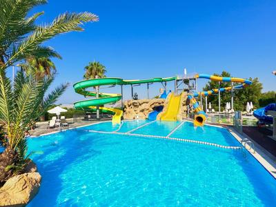 Hotelpool mit Wasserrutschen und Palmen unter klarem blauem Himmel.