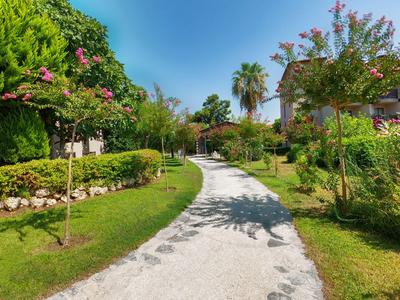 Geschwungener Kiesweg führt durch gepflegte Gartenanlage mit Palmen und blühenden Bäumen.