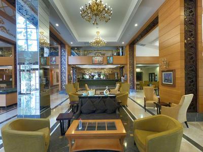 Moderne Hotellobby mit Sesseln, Tischen und Kronleuchtern in warmen Farben.