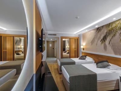 Modern eingerichtetes Hotelzimmer mit Doppelbett, Nachttischen und Palmenmotiv an der Wand.