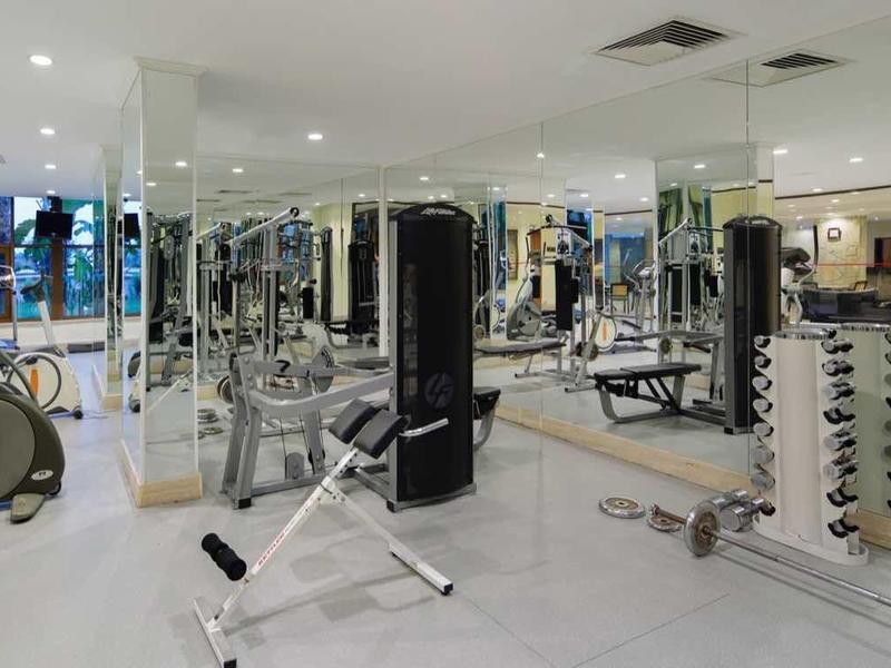 Spacious hotel gym with cardio machines, free weights, and mirrors, featuring a light floor and ceiling lights.