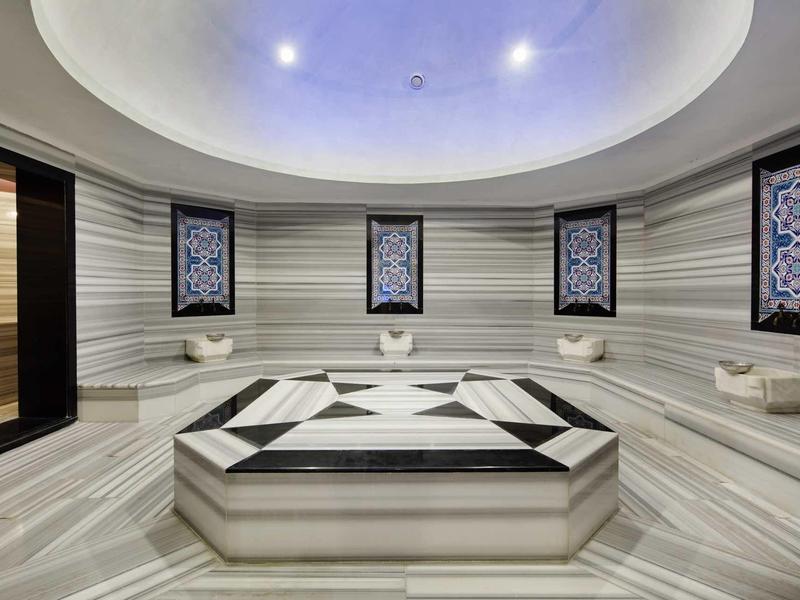 Elegant Turkish bath with marble benches and intricate wall decorations under soft lighting.