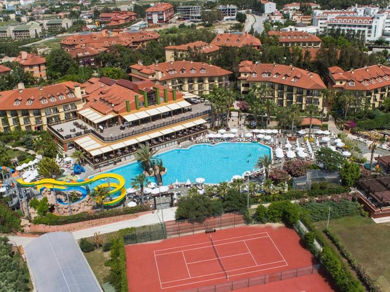 Resort with large pool, water slides, surrounded by red-roofed buildings and tennis courts.