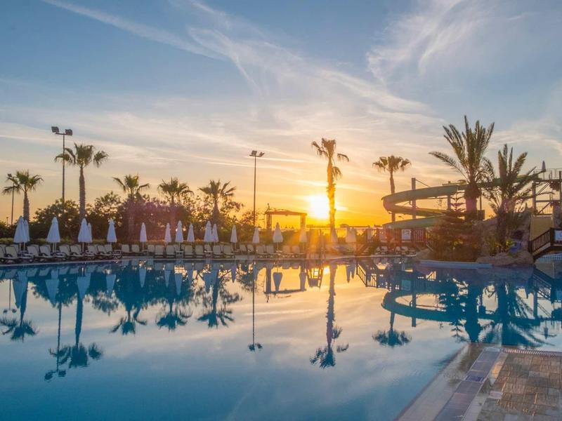 Sunset over a tranquil pool area with palm trees and lounge chairs at a resort.