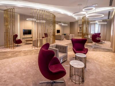 Elegantní hotelová lounge s moderními červenými křesly a zlatými příčkami.