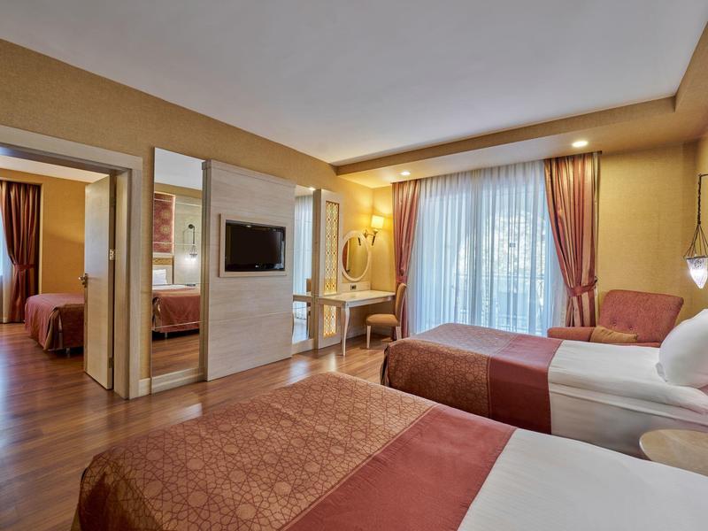 Helles Hotelzimmer mit zwei Einzelbetten, Sesseln und großem Fenster mit Vorhängen.