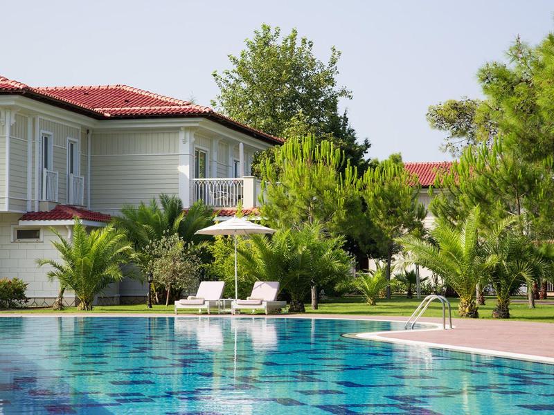 Großes Haus mit rotem Dach, Swimmbad, Liegestühlen und grünen Pflanzen im Garten.