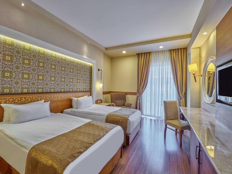 Modernes Hotelzimmer mit zwei Einzelbetten, Schreibtisch und Balkon mit Vorhängen.