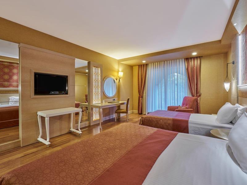 Hotelzimmer mit zwei Doppelbetten, TV, Schreibtisch und großem Fenster mit Vorhängen.