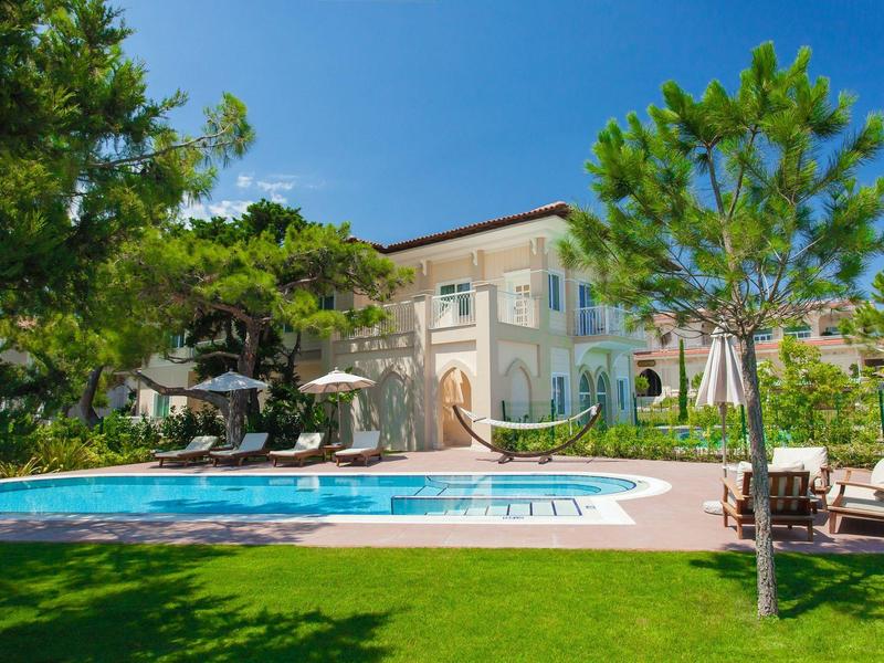 Hotelgebäude mit Swimmingpool, Sonnenliegen und einem Hängesessel unter blauem Himmel
