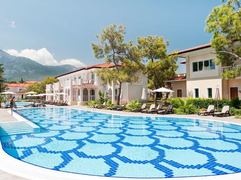 Großer Hotelpool mit geometrischem Muster, umgeben von Liegestühlen und mediterranen Gebäuden.