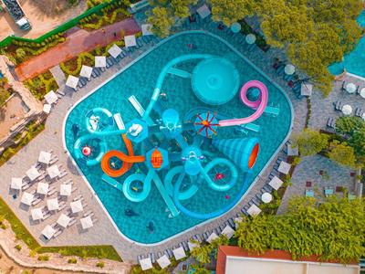 Luftaufnahme eines Pools mit bunten Wasserrutschen, umgeben von Liegestühlen und Bäumen.