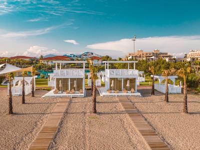 Zwei moderne, weiße Strandpavillons mit Sandwegen und blauen Himmel im Hintergrund.