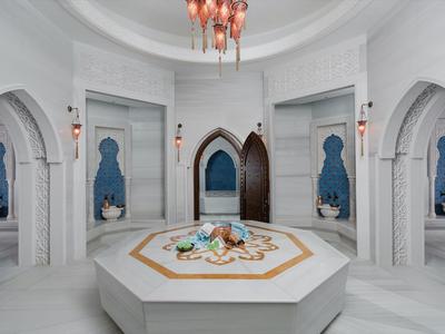 Eleganter, weißer Marmorinnenraum mit zentralem Brunnen und Bogenfenstern in einem Hotel.