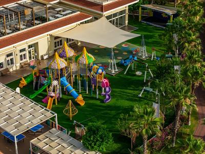 Spielplatz mit bunten Klettergerüsten und Rasenfläche neben einem Hotelgebäude.