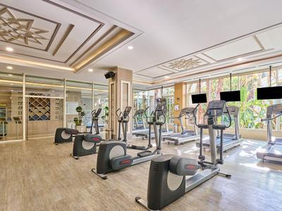 Helles Fitnessstudio mit Cardiogeräten vor großen Fenstern und Aussicht auf Grünflächen.
