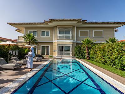 Modernes Haus mit Pool und Liegestühlen, bewachsene Hecke und Person in Bademantel.