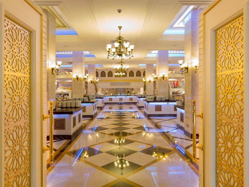 Elegant hotel lobby with ornate golden doors, shiny tiled floor, and chandelier lighting.