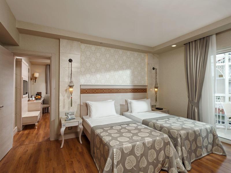 Hotel room with two twin beds, bedside tables, wooden floor, and a balcony with curtains.