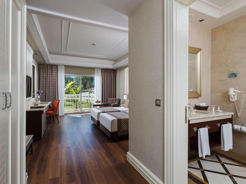 Modern hotel room with twin beds, wooden floor, and bathroom with towels and hairdryer.