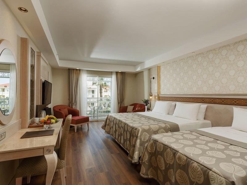 Hotel room with two beds, a desk, chairs, and balcony with natural light.