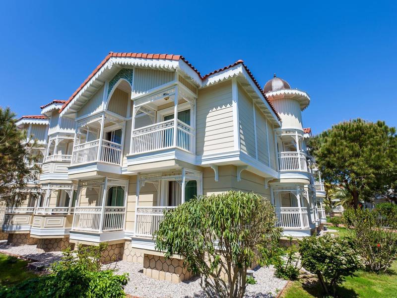 Modern white vacation building with balconies under a clear blue sky surrounded by greenery.
