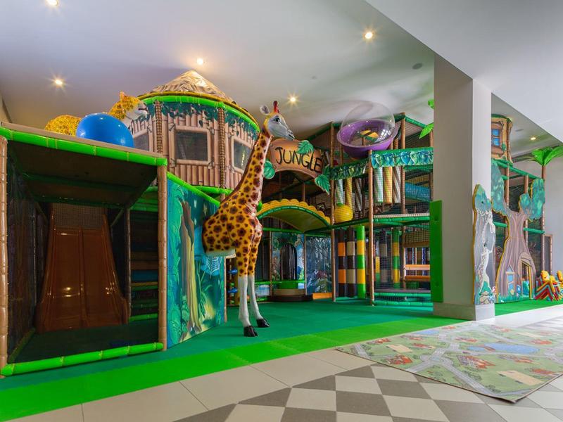 Indoor kids' play area with jungle theme, colorful structures, and a giraffe figure.