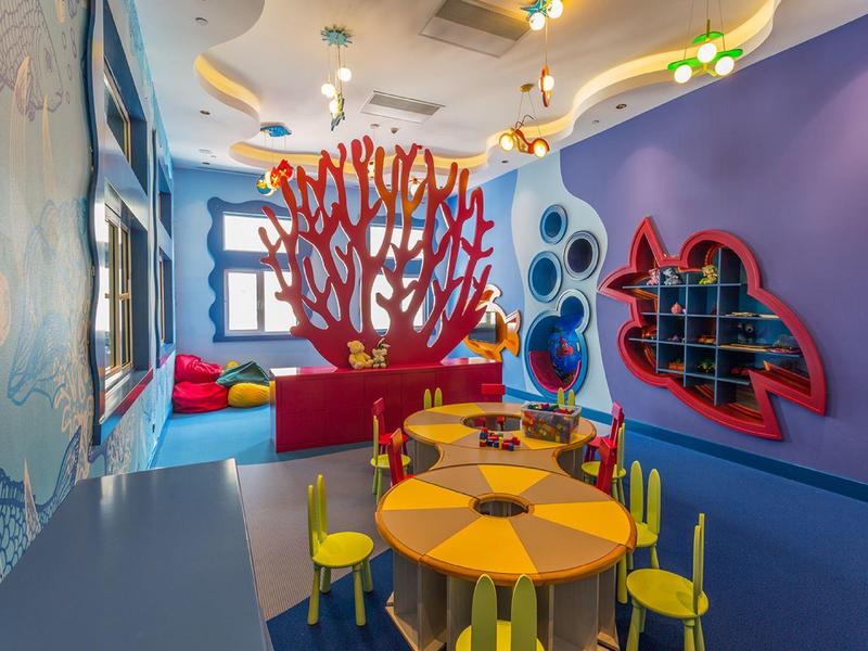 Colorful kids' playroom with coral-shaped pink structure, yellow table and chairs, and blue walls.
