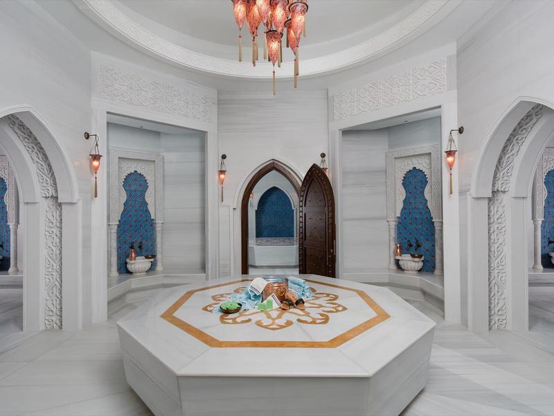 Luxurious white marble Turkish bath interior with arches, blue tile artwork, and central octagonal platform.