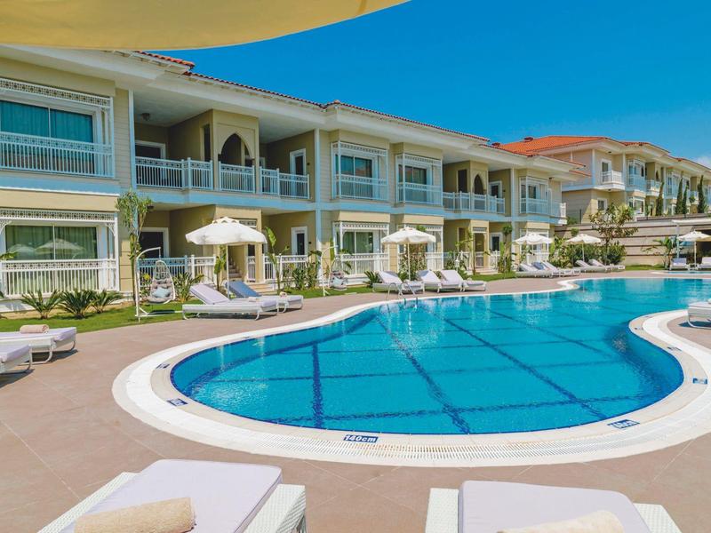 Curved outdoor pool with lounge chairs and white umbrellas by a two-story hotel building.
