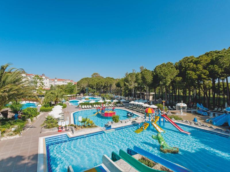 Resort pool area with slides, palm trees, and sun loungers under a blue sky.